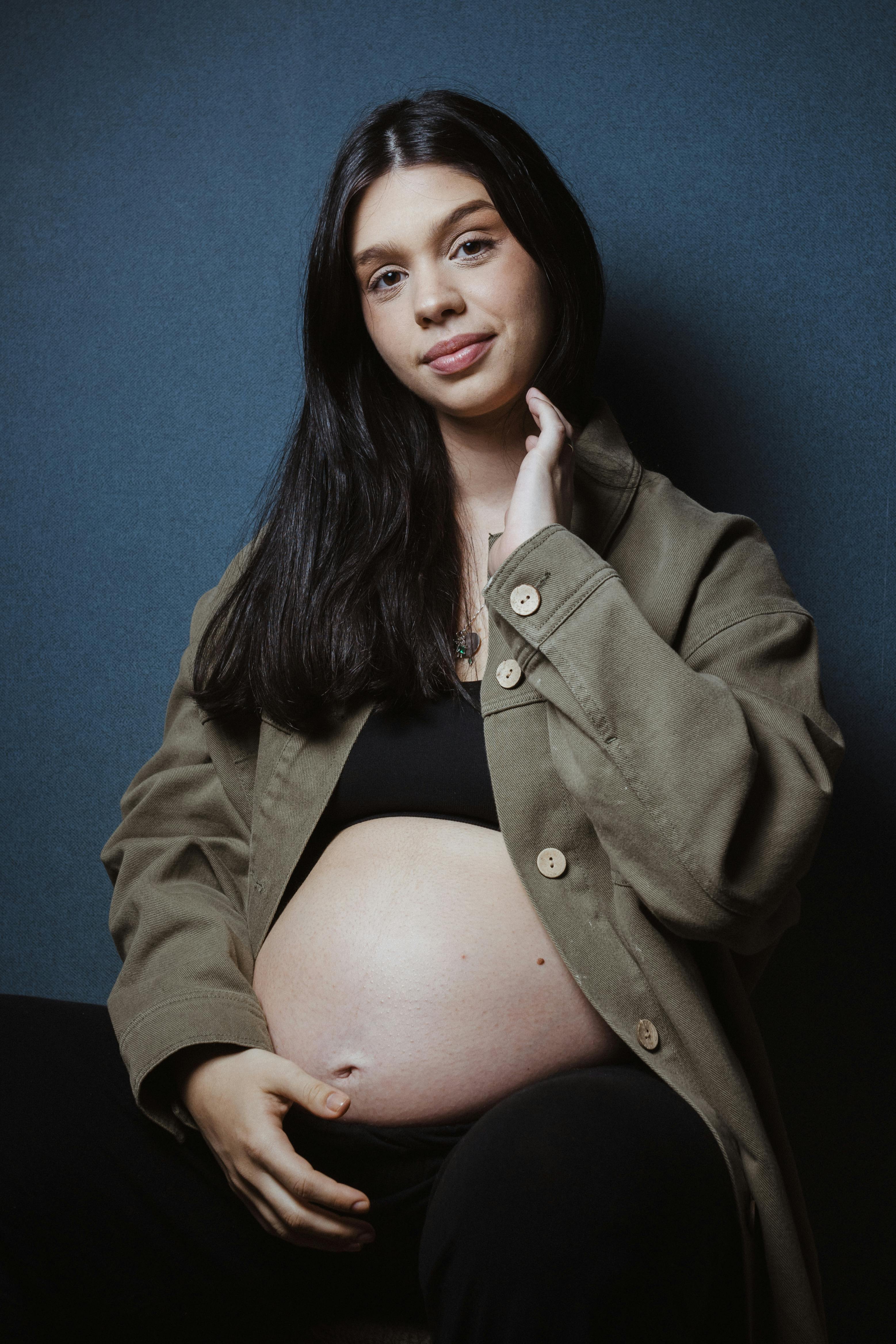 a pregnant woman in a black coat posing for a portrait