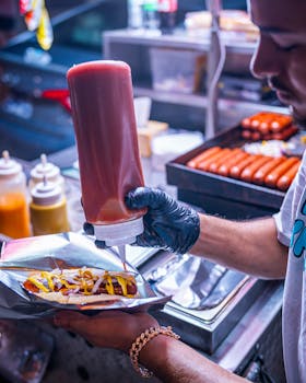 Street food vendor adds ketchup and mustard to a hot dog in Nashville, TN at night.