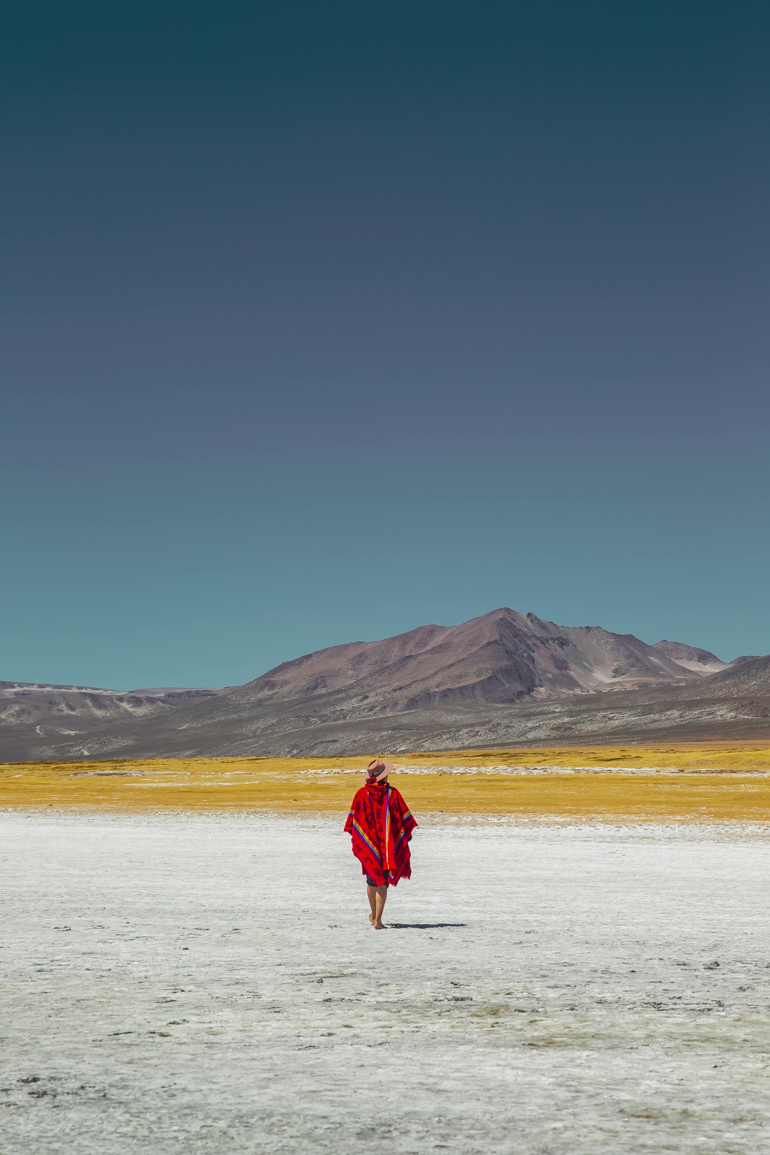 A solitary person in vibrant attire walks across the remote desert landscape of Salinas Huito, Arequipa, Peru.