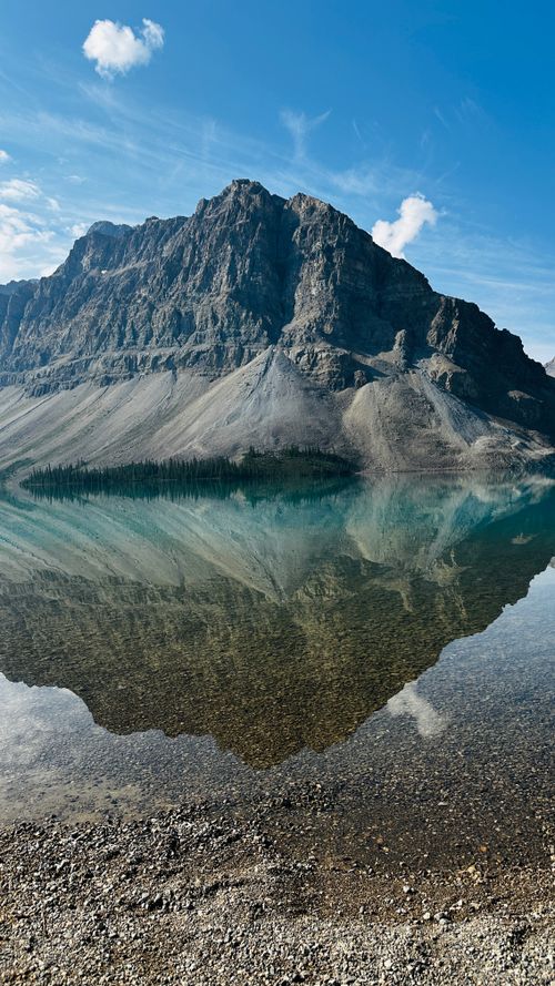 Free A breathtaking view of a mountain reflected in a serene lake under a clear blue sky. Stock Photo