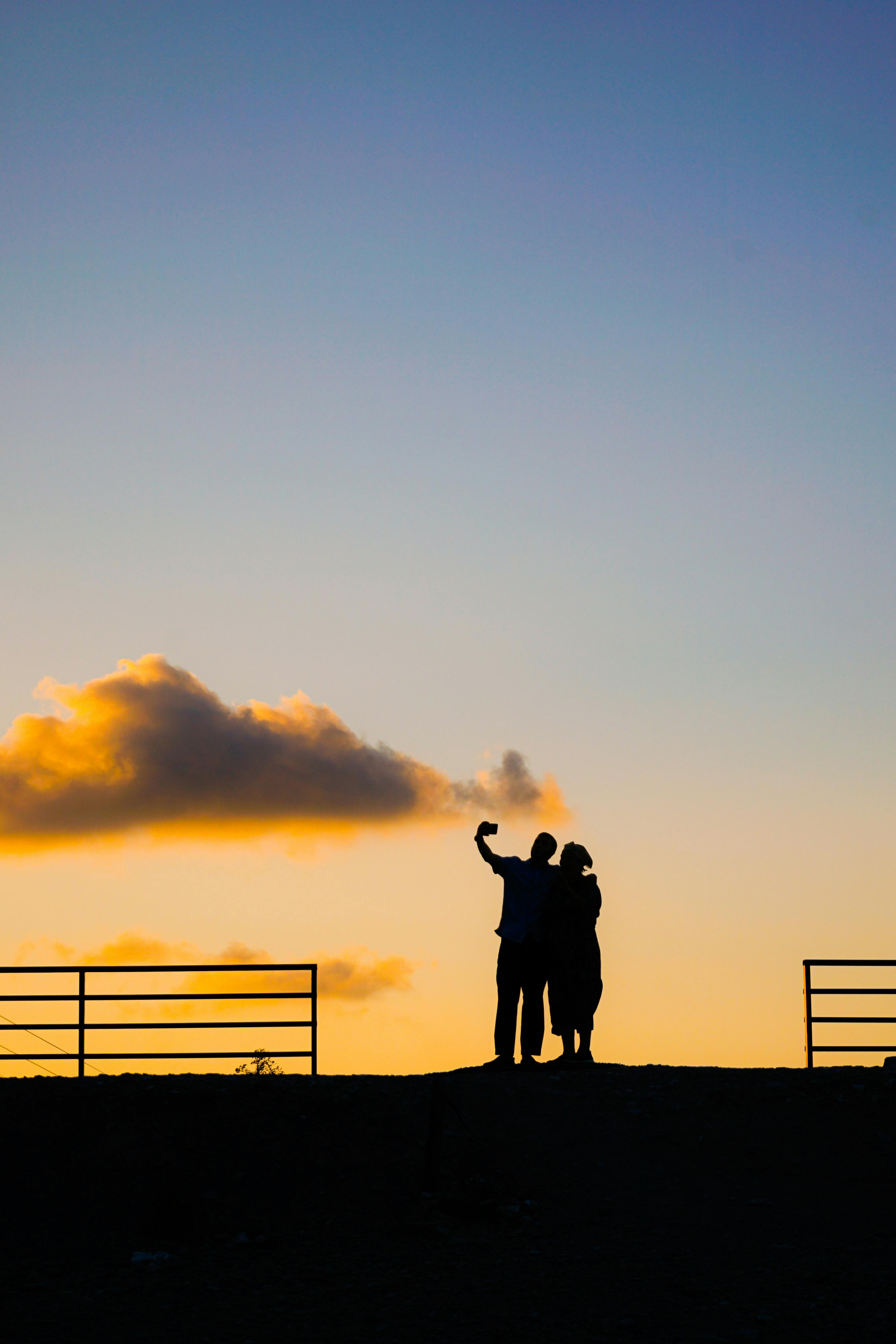 A silhouetted couple takes a selfie against a colorful sunset sky. Perfect for themes of love and travel.