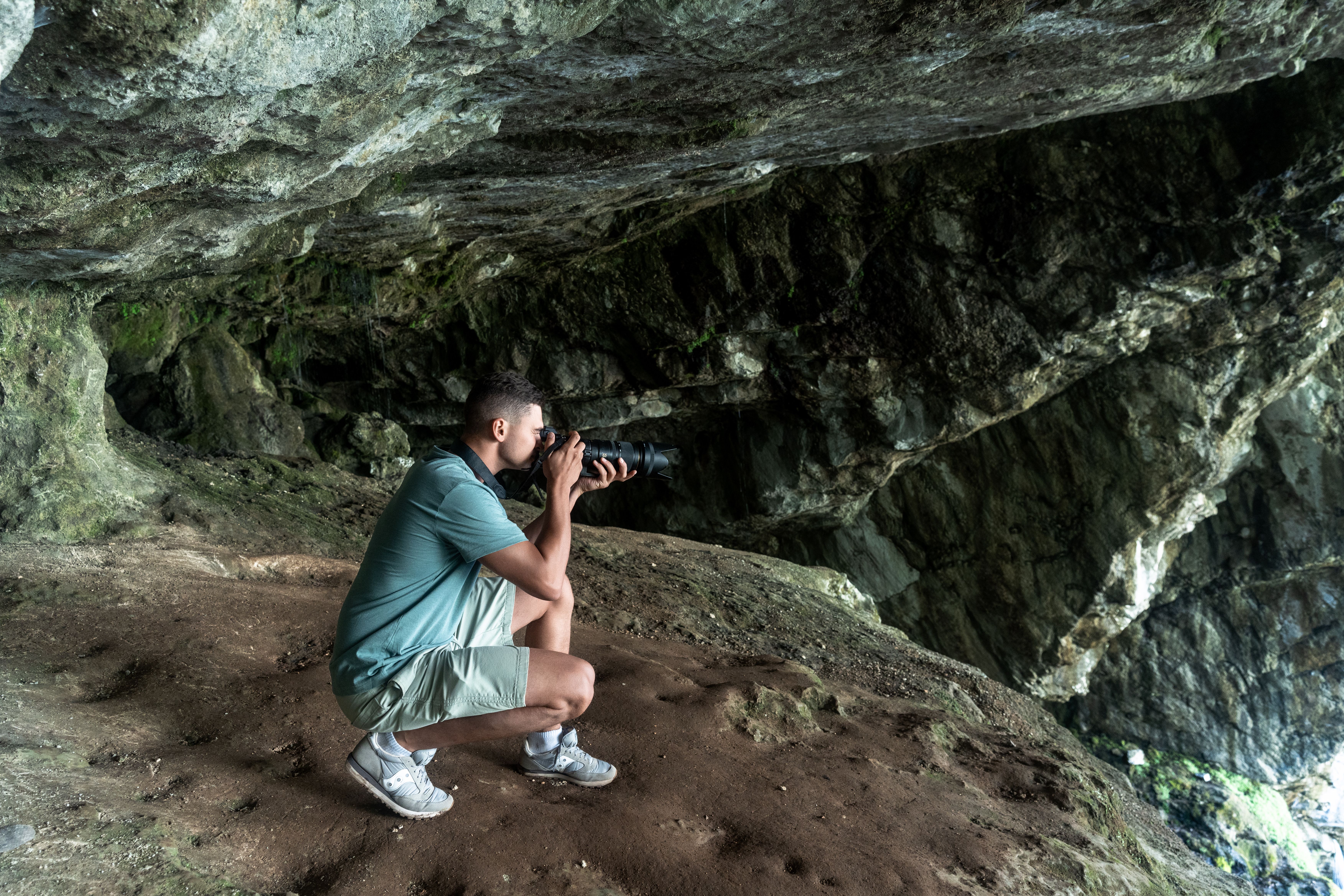 Photographer crouching inside a dimly lit cave, capturing nature's beauty in Гагра.