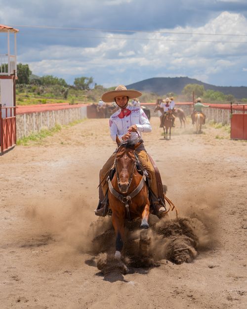 Free Charro skillfully maneuvers horse in a vibrant Mexican rodeo scene. Stock Photo