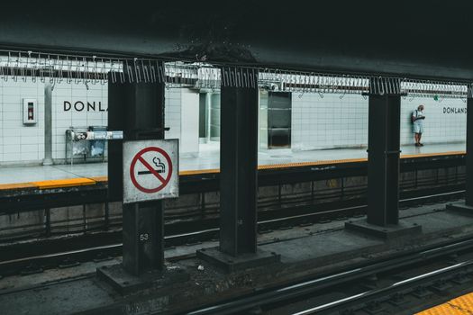 No smoking sign and commuter on Toronto's Donland subway station platform, showcasing urban transit infrastructure.
