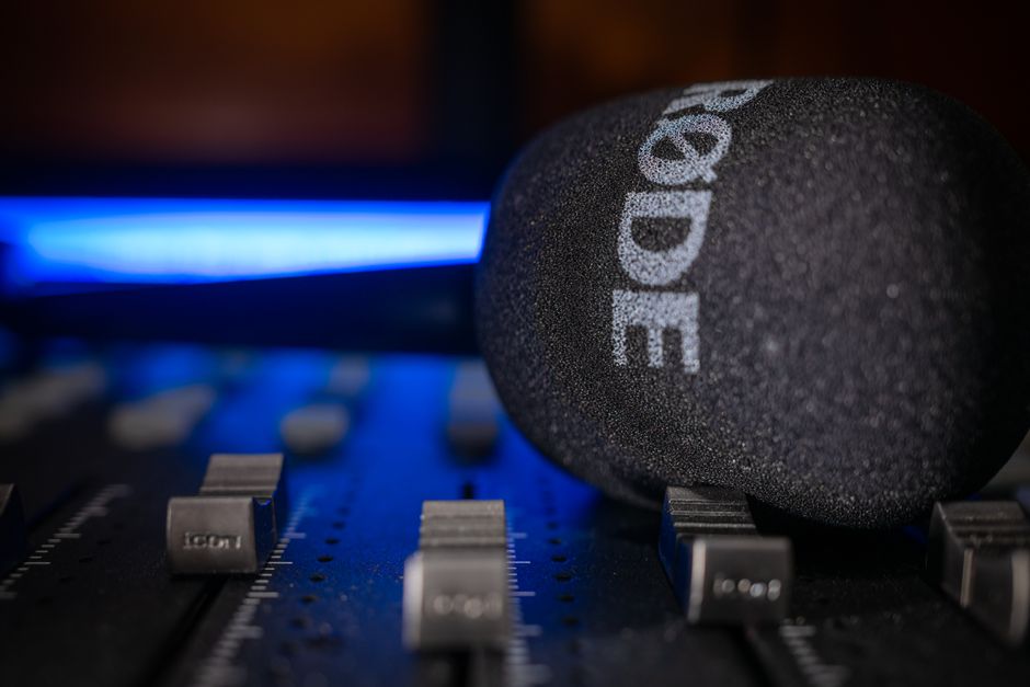 A detailed close-up of a RODE microphone resting on an audio mixer board with blue lighting in Detroit studio.