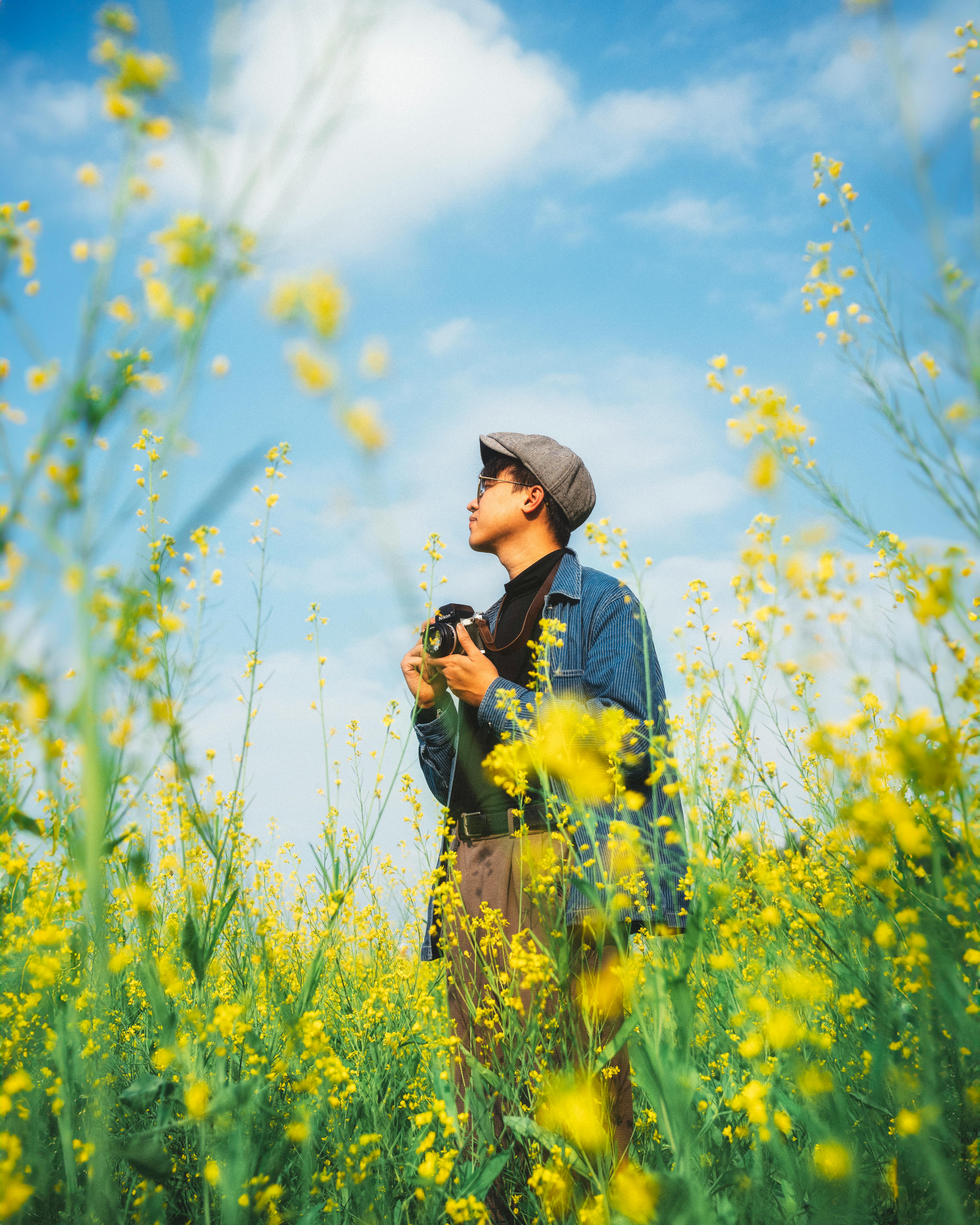 A man with a camera stands amid vibrant yellow flowers in Hanoi, showcasing joy and freedom in nature.