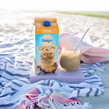 Chilled caramel macchiato iced coffee on a serene beach setting, perfect for a summer day.
