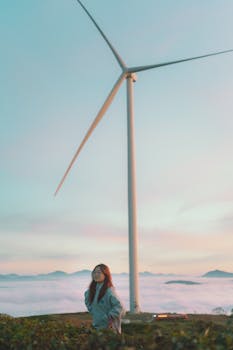 A young woman stands near a towering wind turbine against a picturesque sunset sky in Dalat, Vietnam.