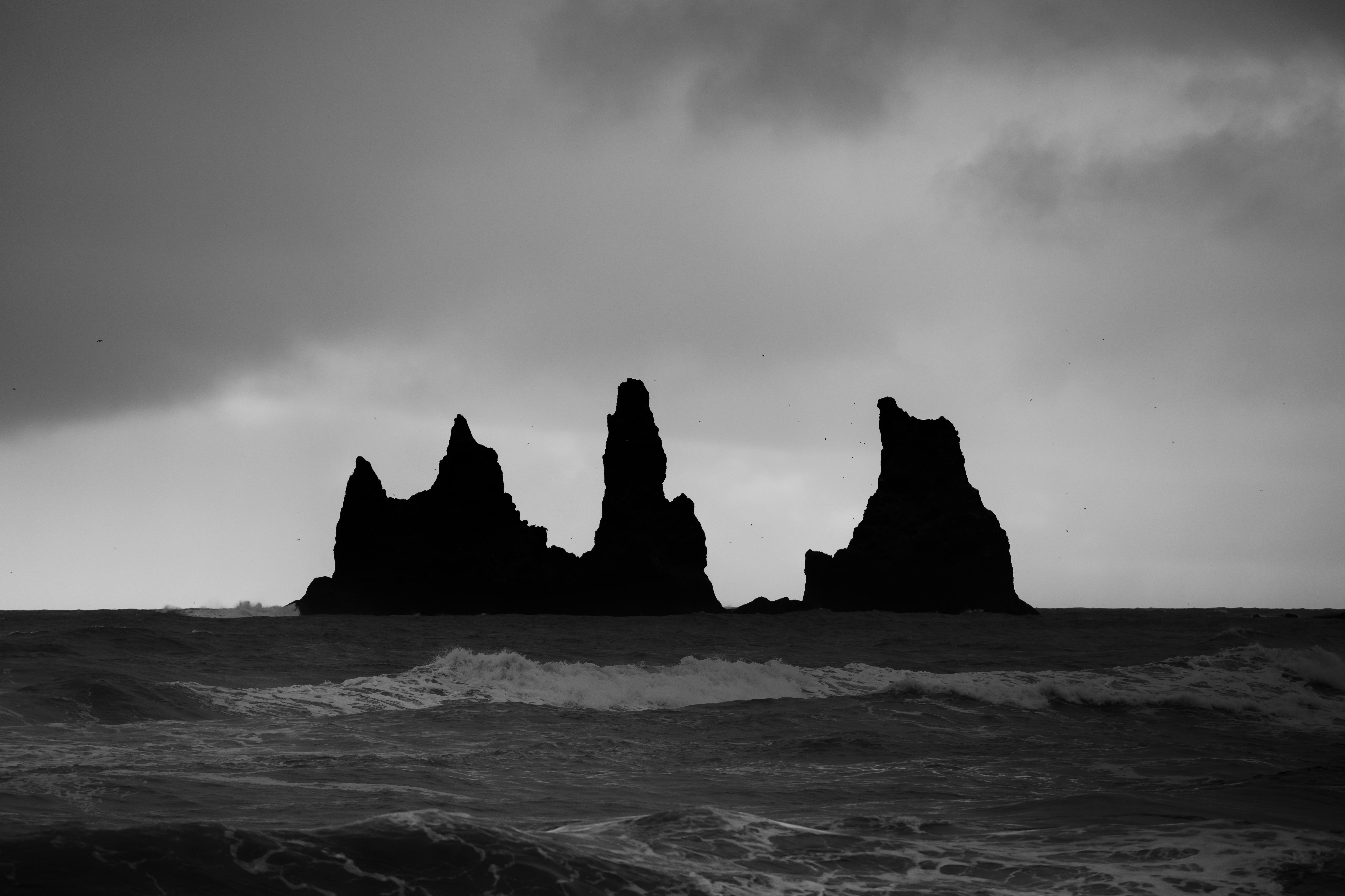 Moody monochrome view of ocean waves against rock formations under stormy sky.