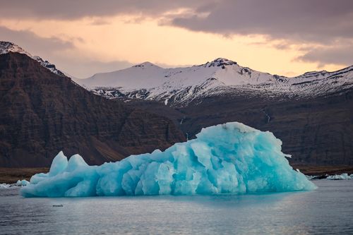 Free A stunning icy landscape with a blue iceberg against snow-capped mountains at sunset. Stock Photo