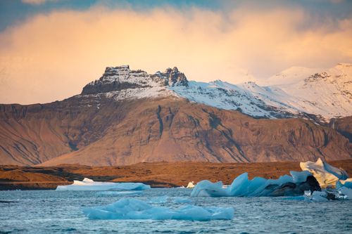 Free Breathtaking view of icy waters and mountains under a glowing sunset sky. Stock Photo