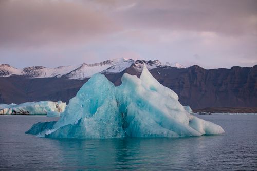 Free Iceberg in serene Icelandic waters with snowy mountains, symbolizing climate change. Stock Photo