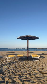 Relaxing beach view in Emilia-Romagna with loungers and umbrella under a clear sky.
