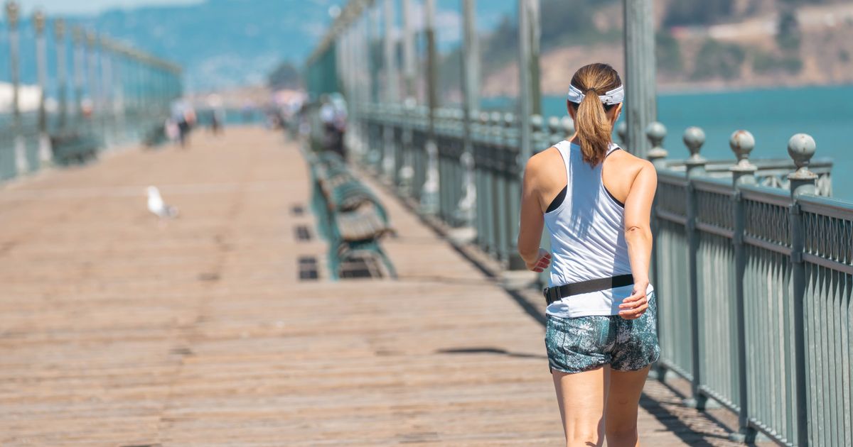 A woman jogging along a sunny seaside pier wearing a slim black running belt