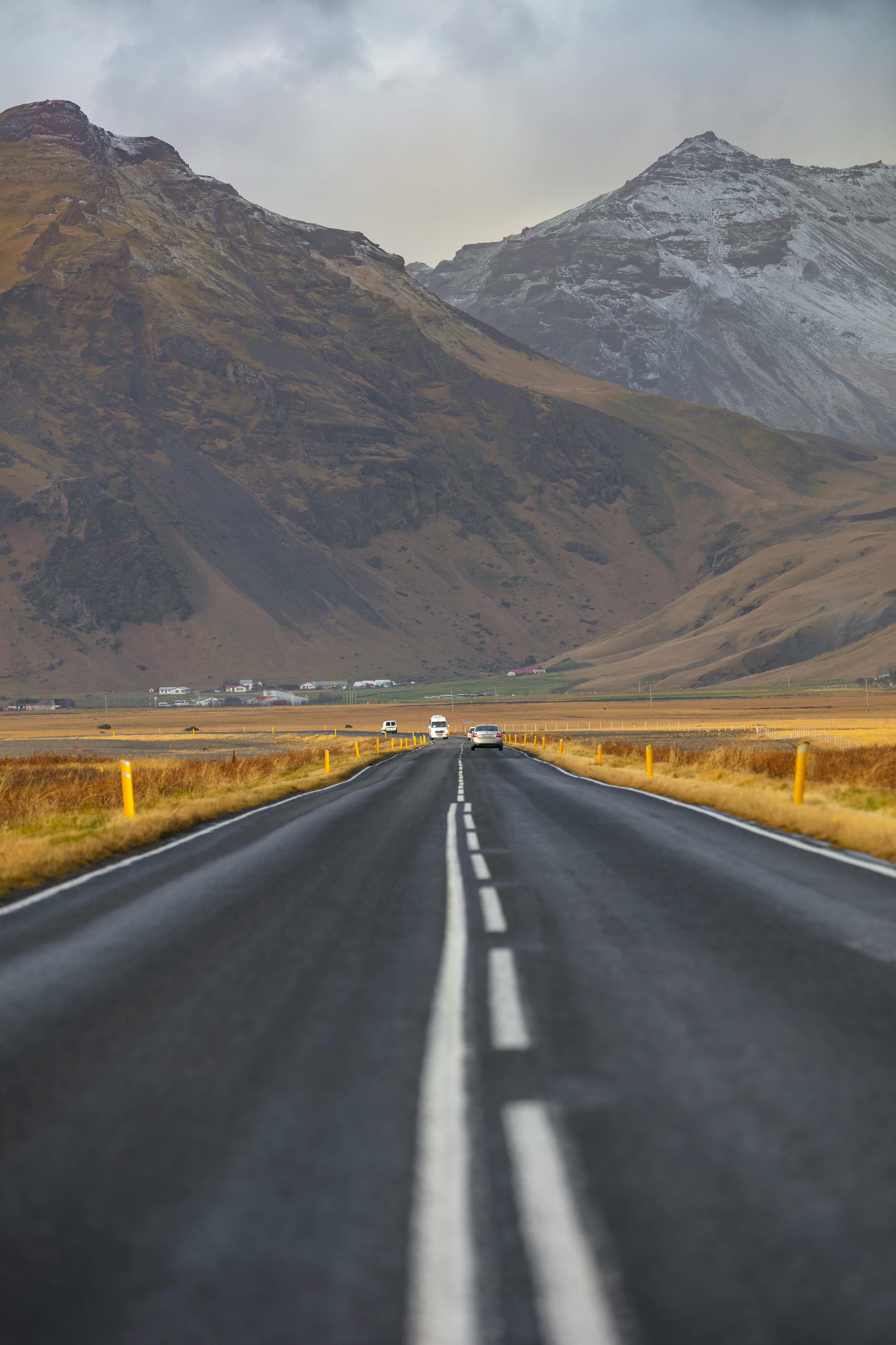 Explore the beauty of a remote road leading to majestic, snow-capped mountains on a cloudy day.