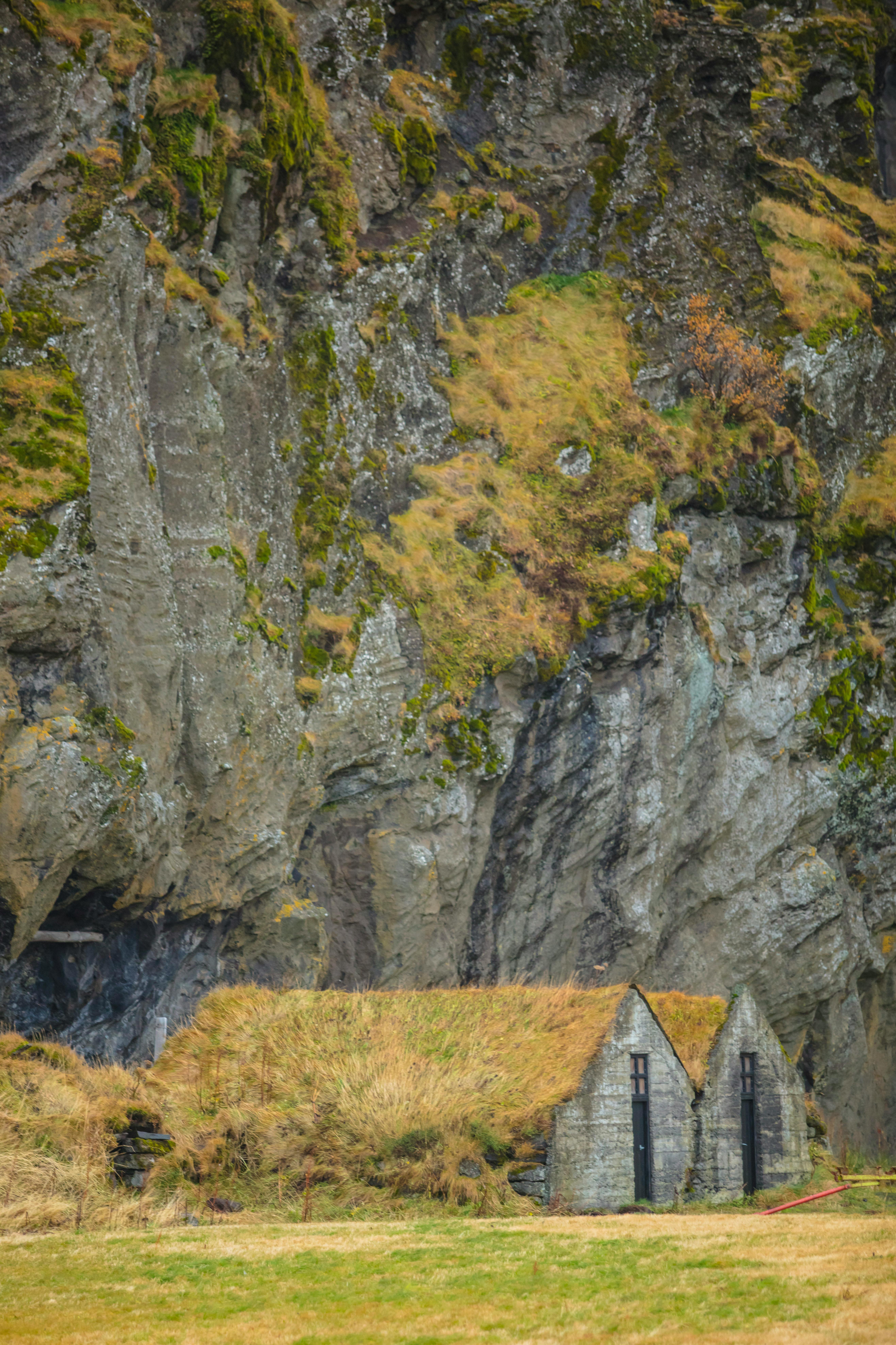 Cozy stone cottages with grass roofs perched against a rugged cliff in rural landscape.