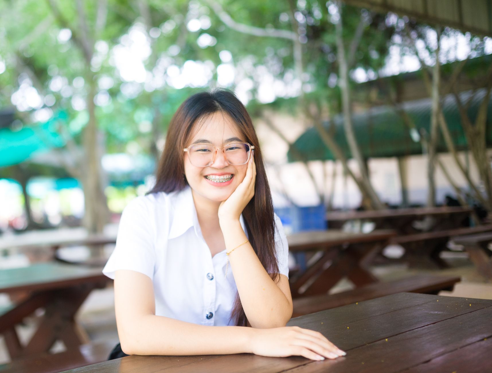 Happy young woman with glasses and braces enjoying leisure time outside at picnic table.