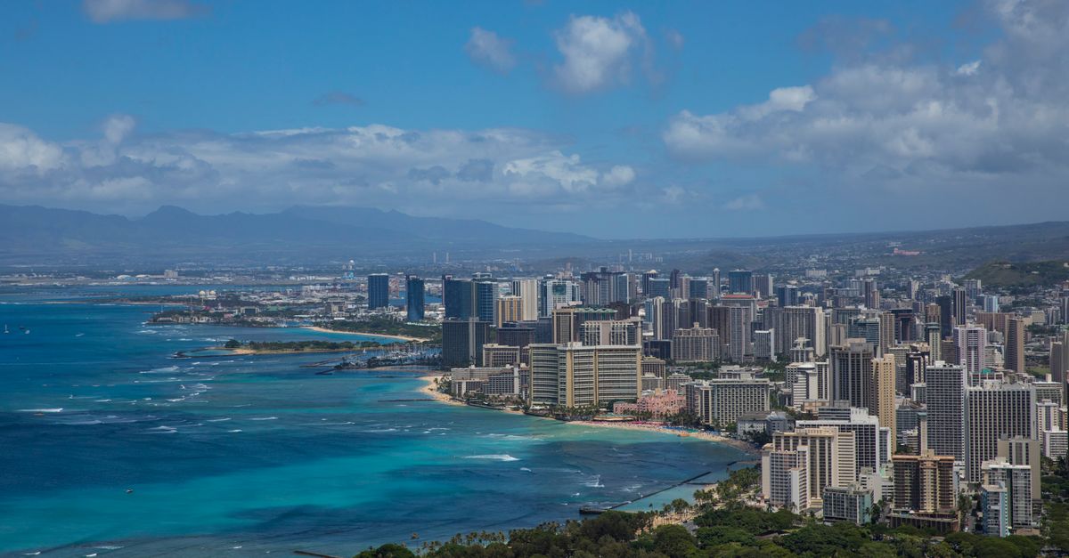 Photo by Stephen Leonardi Stunning aerial view of Honolulu's skyline with vibrant ocean hues and lush greenery.