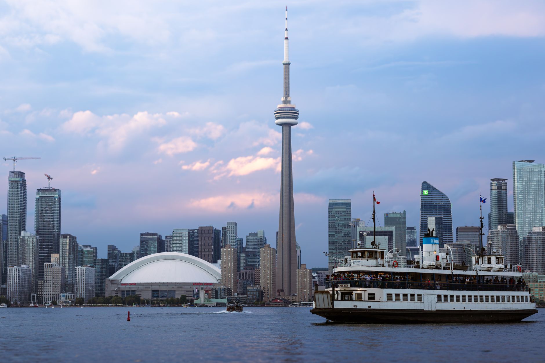 A beautiful view of Toronto's skyline featuring the CN Tower and a ferry on Lake Ontario during sunset.