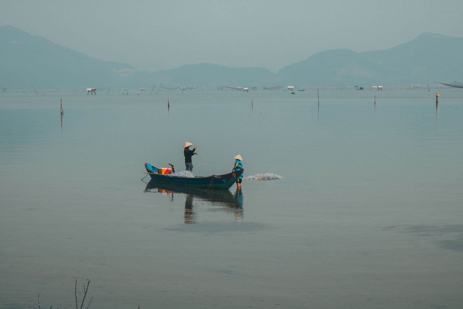 Fishermen on a boat in the serene waters of Hue, Vietnam, casting nets at dawn.