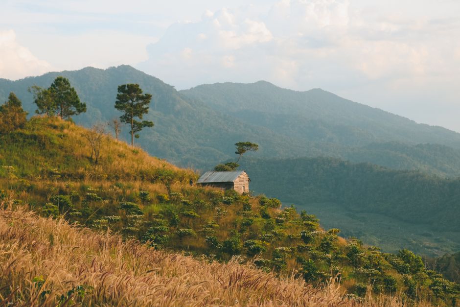 Tranquil rural scene capturing rolling hills and a lone hut in Kon Tum, Vietnam at sunrise.