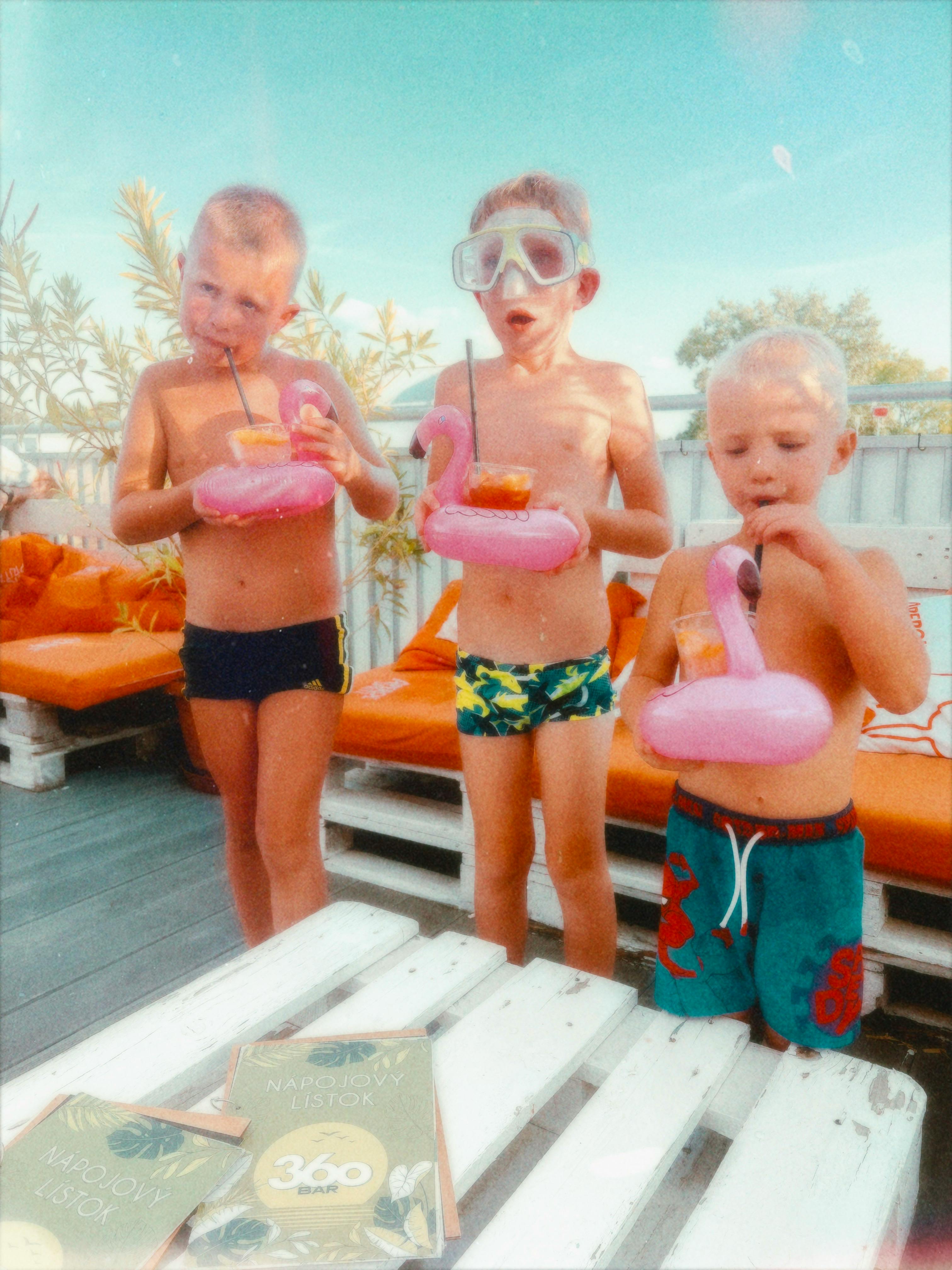 Free Three kids sipping fruity drinks with pool inflatables on a sunny summer day. Stock Photo