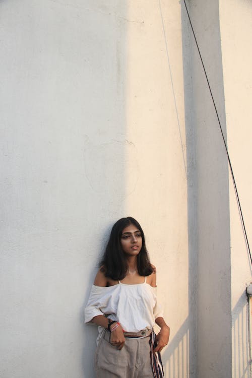 Woman in White Off-shoulder Top Leaning on Wall