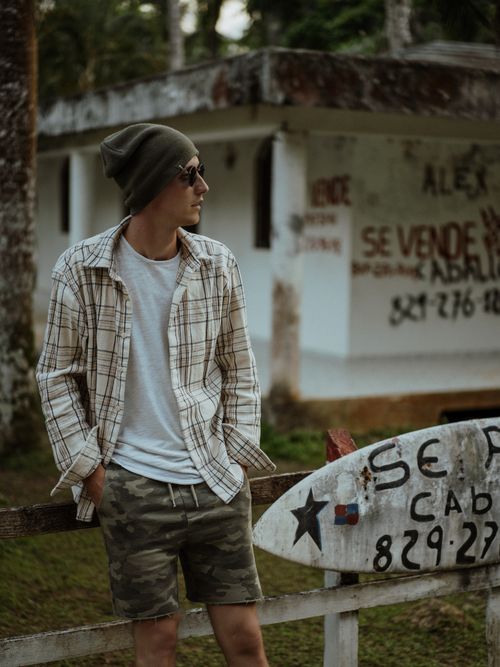 Free Man in casual wear standing by a rustic fence in Las Terrenas, capturing a laid-back lifestyle. Stock Photo