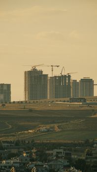 Distant view of urban construction and cranes under a golden sunset, with a cityscape backdrop.