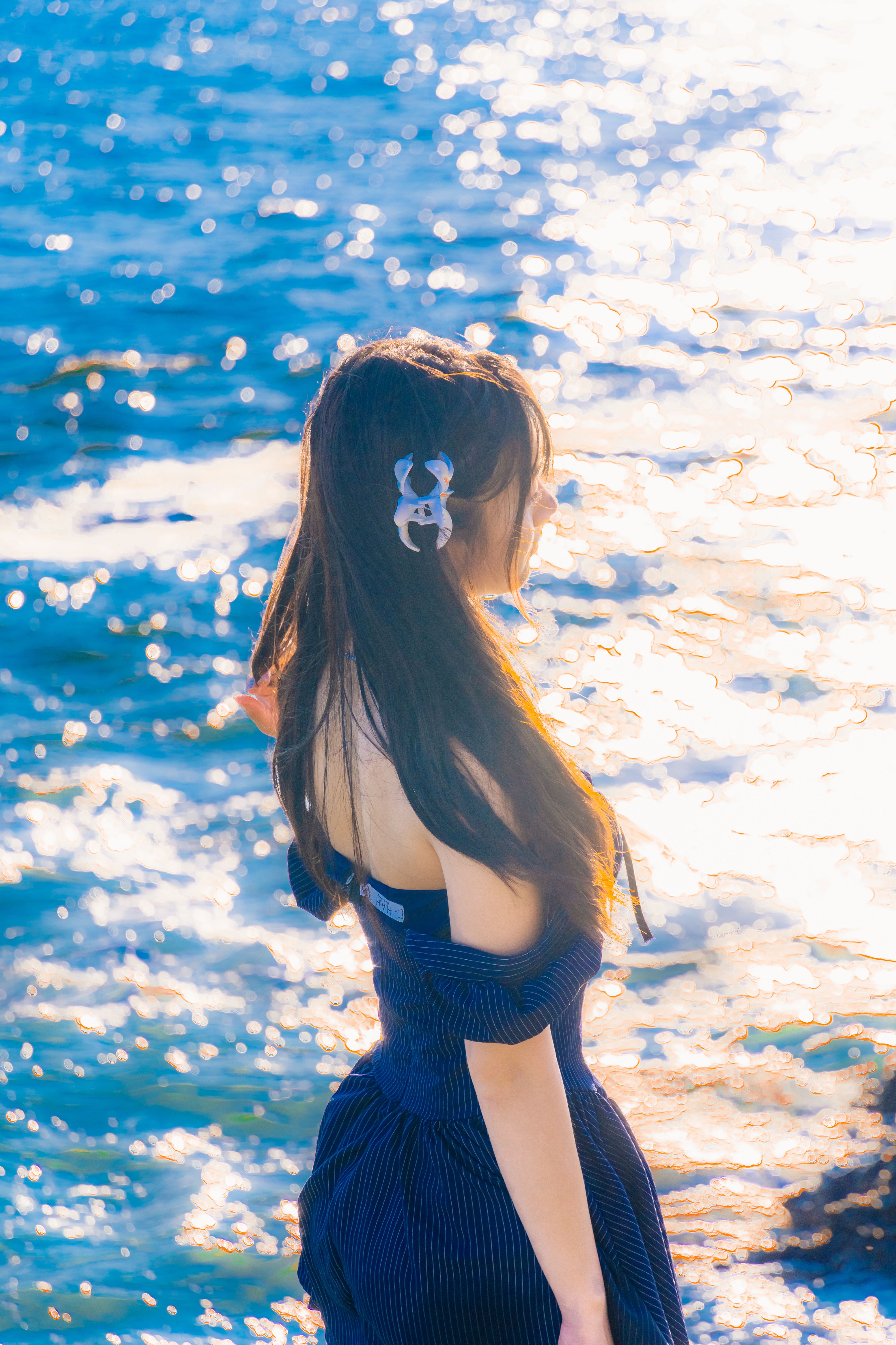 A woman in a summer dress overlooking the ocean, illuminated by the setting sun.