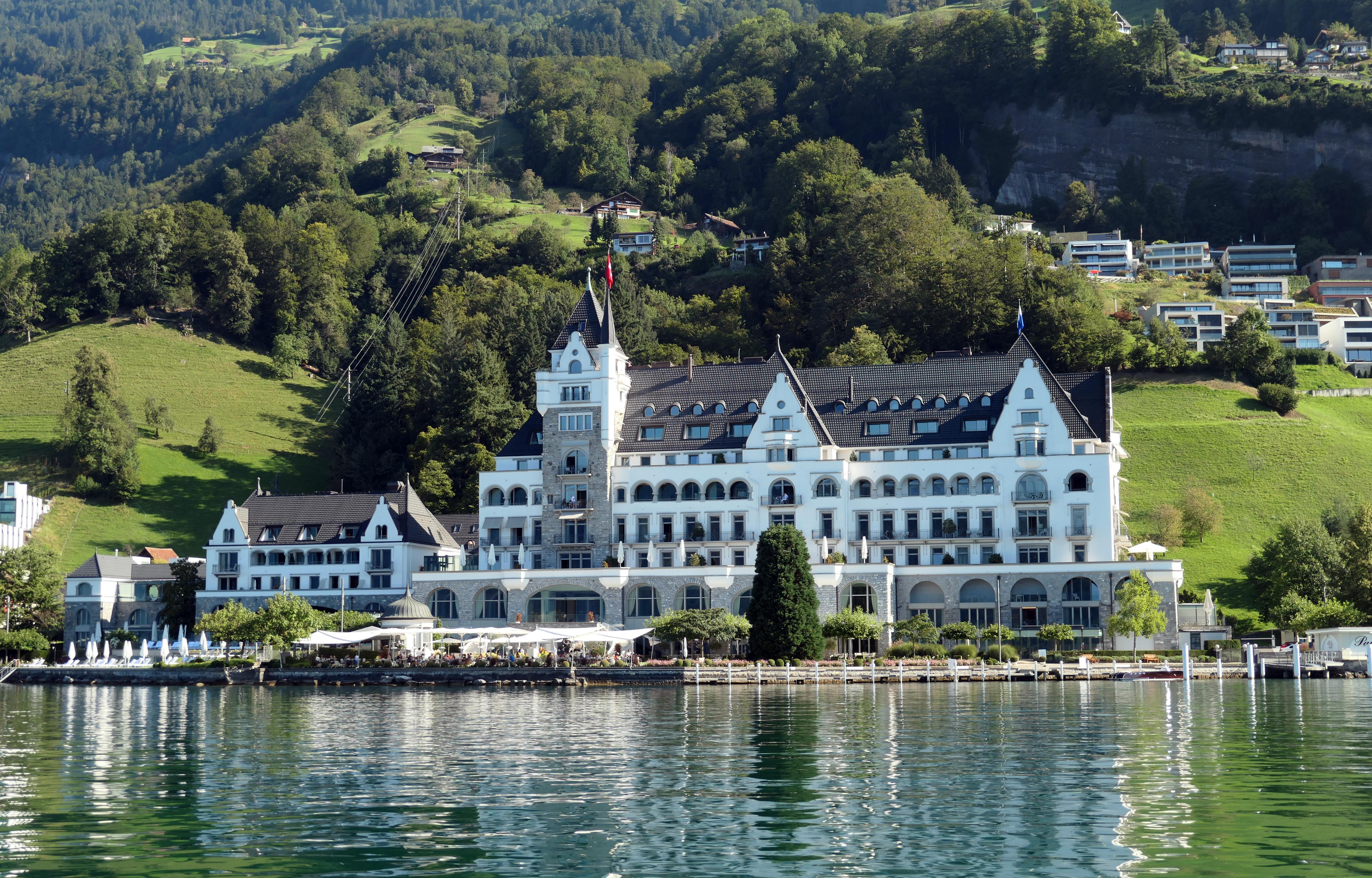 Elegant lakeside hotel in Vitznau, Switzerland with scenic mountainous backdrop and tranquil reflections.