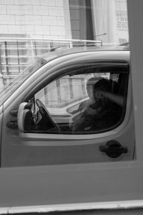 Free Black and white image of a person driving a car, reflecting urban life through a window. Stock Photo