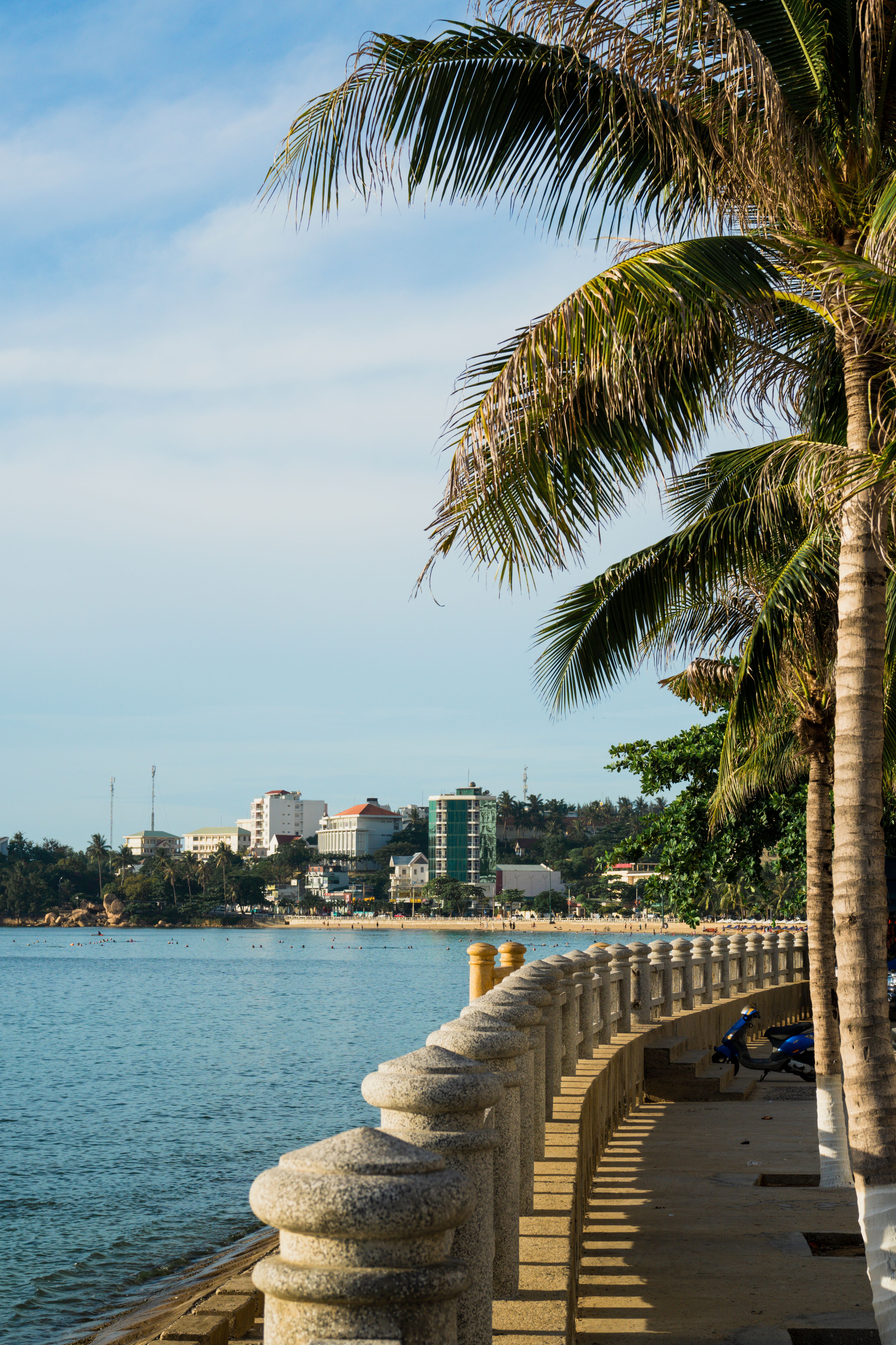 Luxury beachfront hotels and resorts in Bai Chay, Ha Long, palm-lined boulevard, modern architecture, sunset over the bay, travelers strolling, highly detailed realistic travel scene