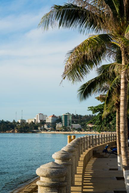 Luxury beachfront hotels and resorts in Bai Chay, Ha Long, palm-lined boulevard, modern architecture, sunset over the bay, travelers strolling, highly detailed realistic travel scene