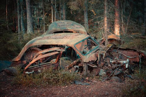 Free Abandoned vintage car wreckage covered in rust in a forest setting, conveying a sense of decay. Stock Photo