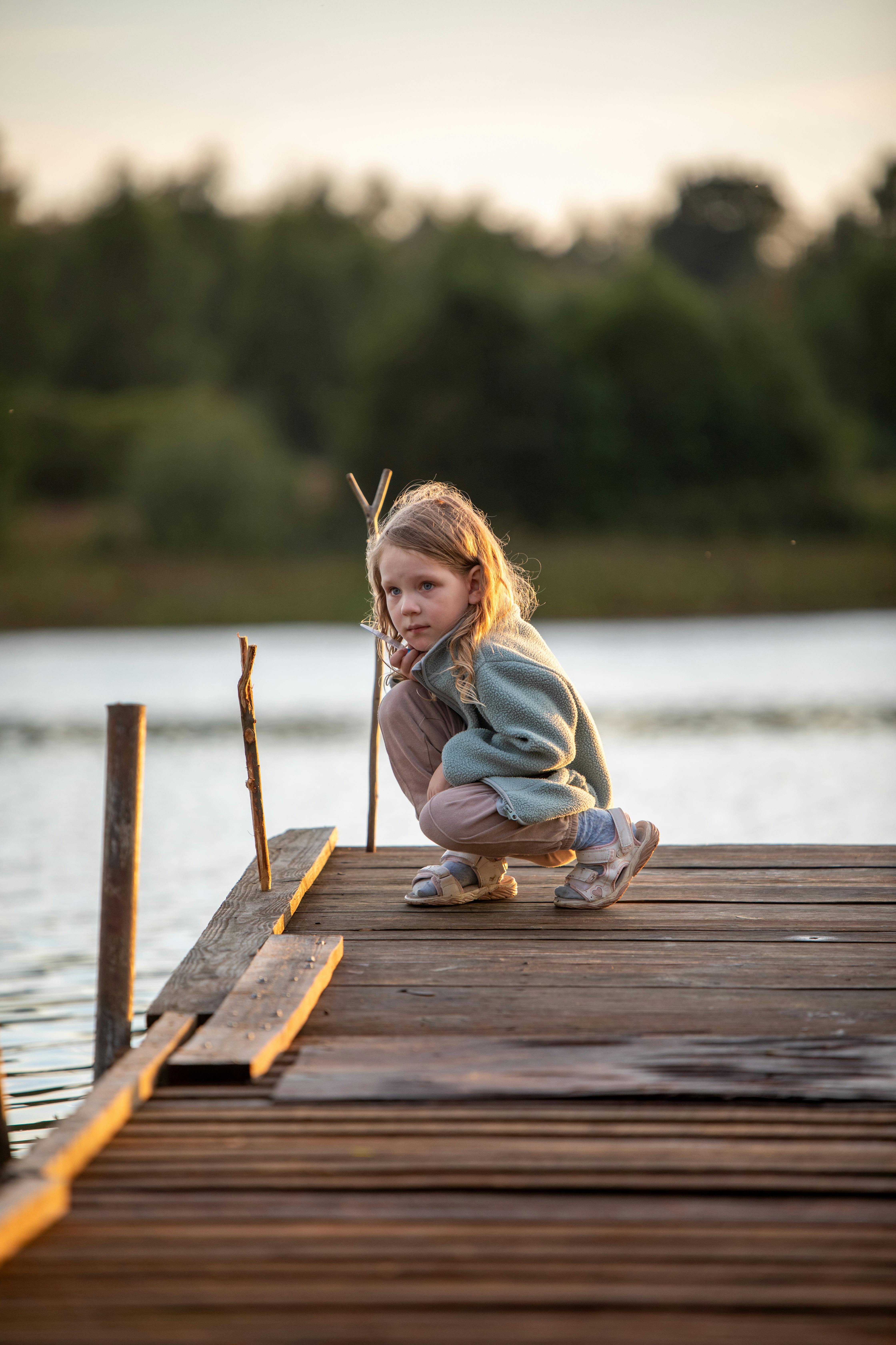 a little girl crouching on a dock near a lake