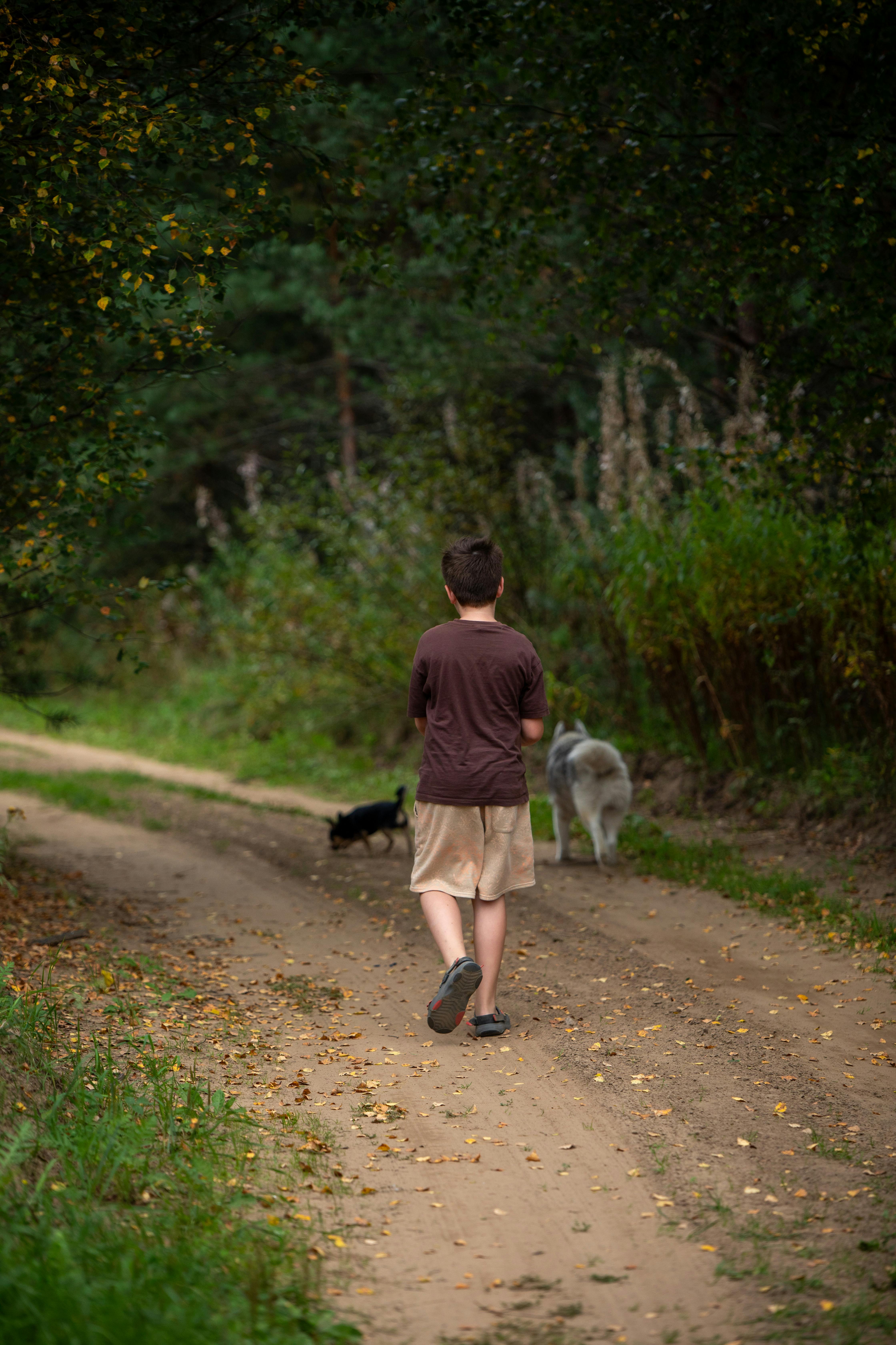 A boy walking down a dirt road with a dog