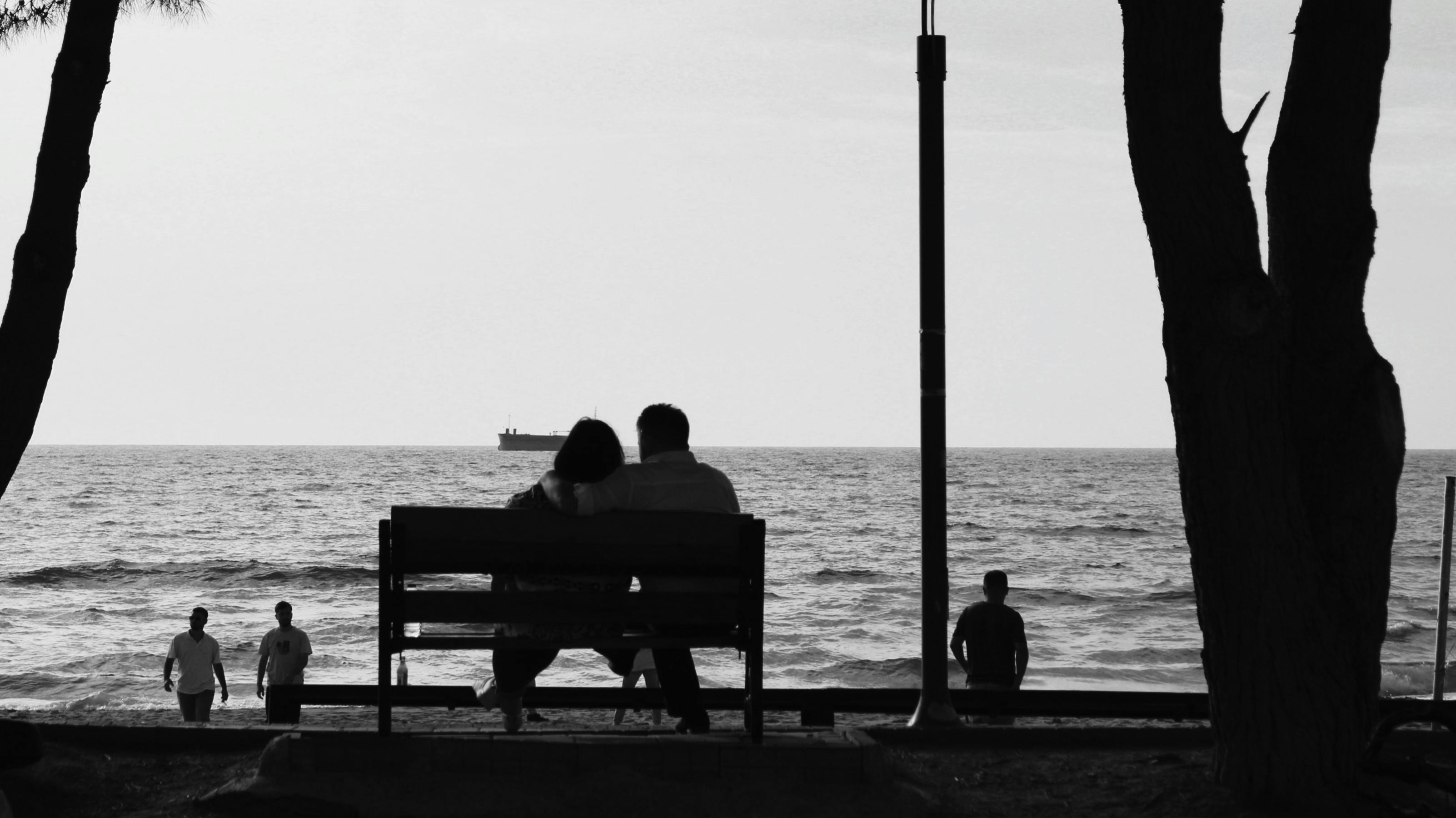 a couple sitting on a bench by the ocean