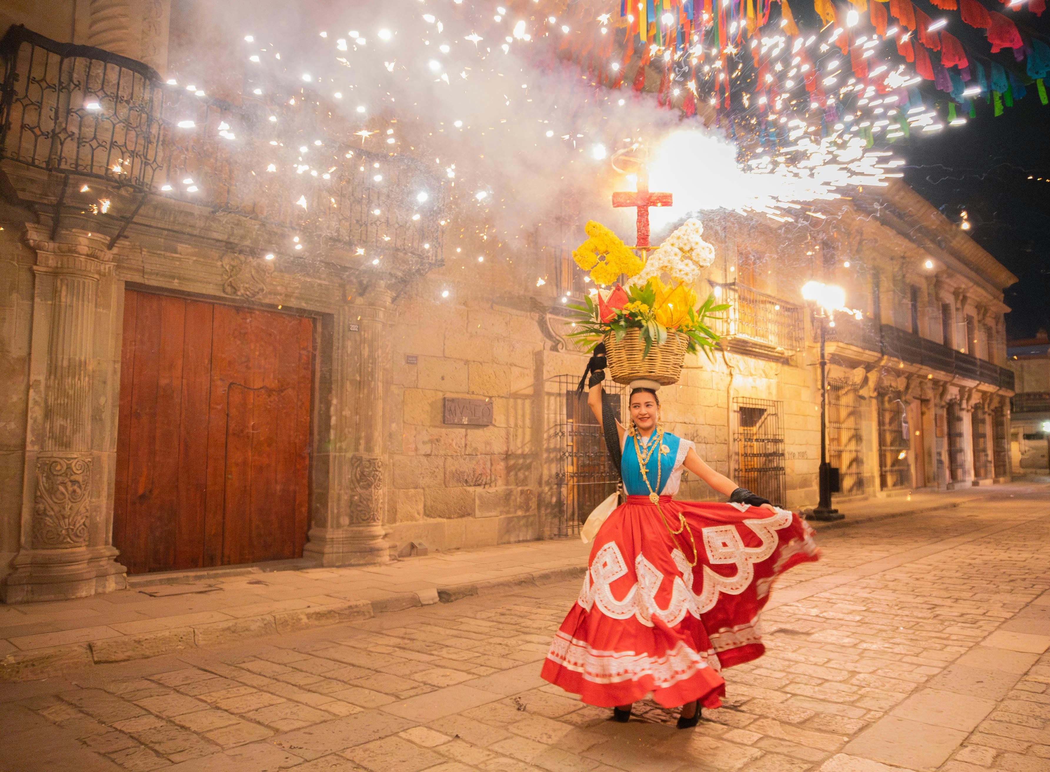 Woman in traditional Oaxacan embroidered dress carries a basket of flowers during Guelaguetza festival cultural parade in Oaxaca Mexico