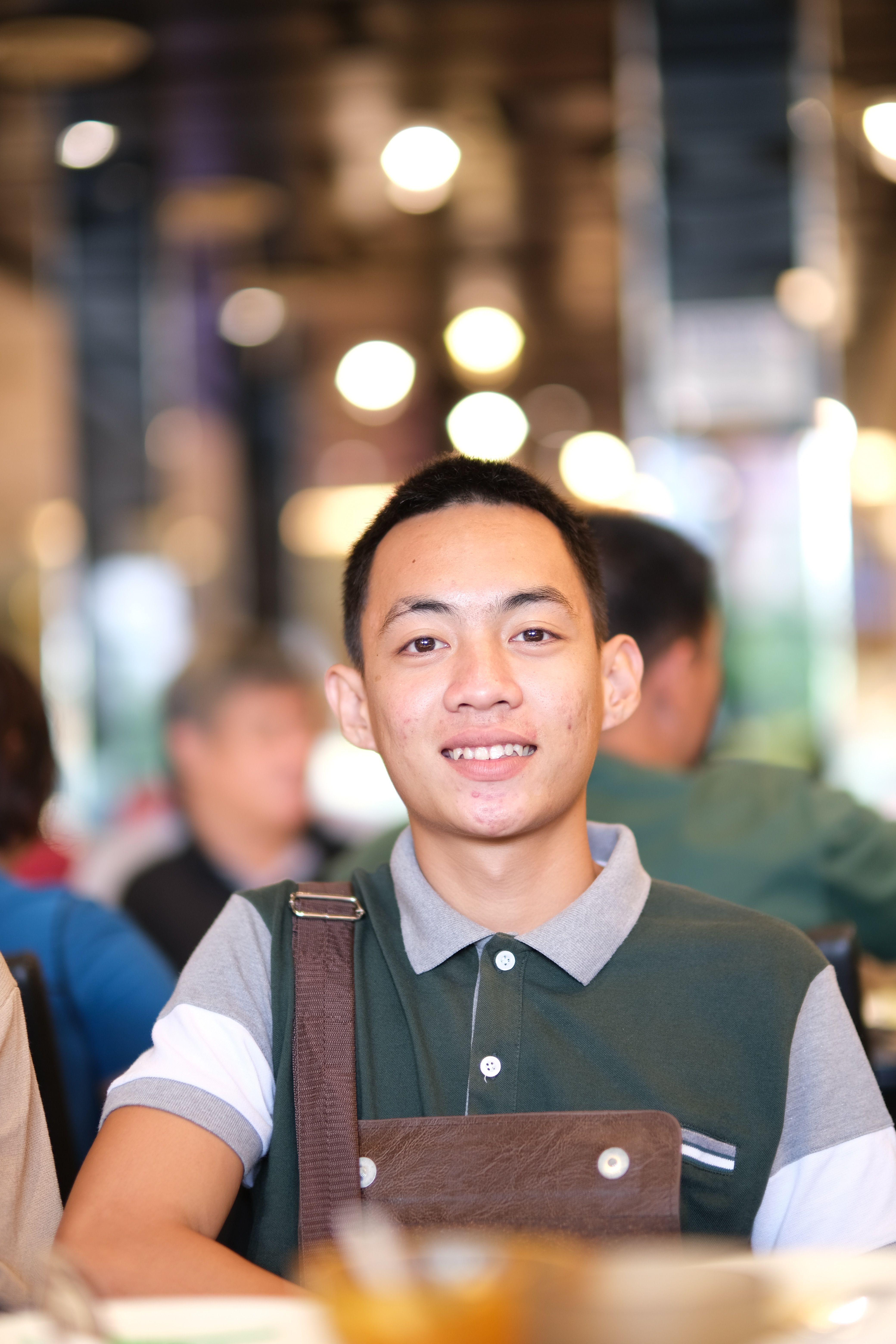 Young barista smiling in a busy modern coffee shop setting with a blurred energetic background.