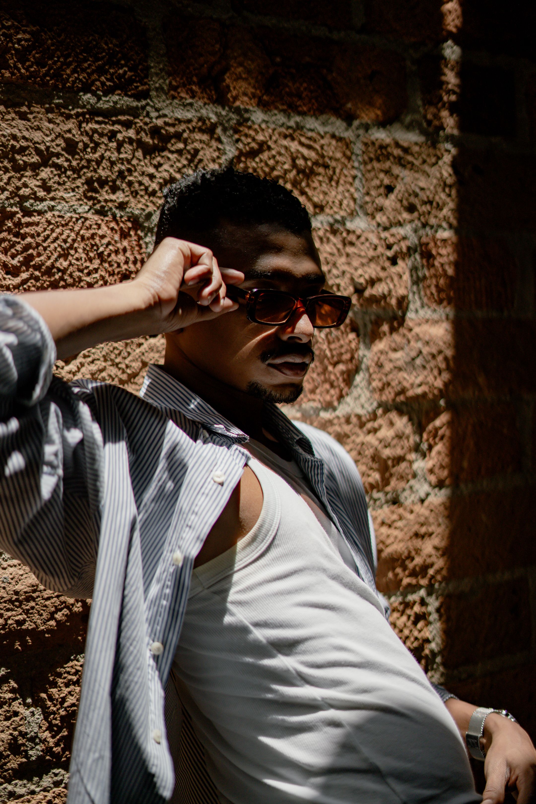 Stylish man in sunglasses leaning on sunlit brick wall · Free Stock Photo
