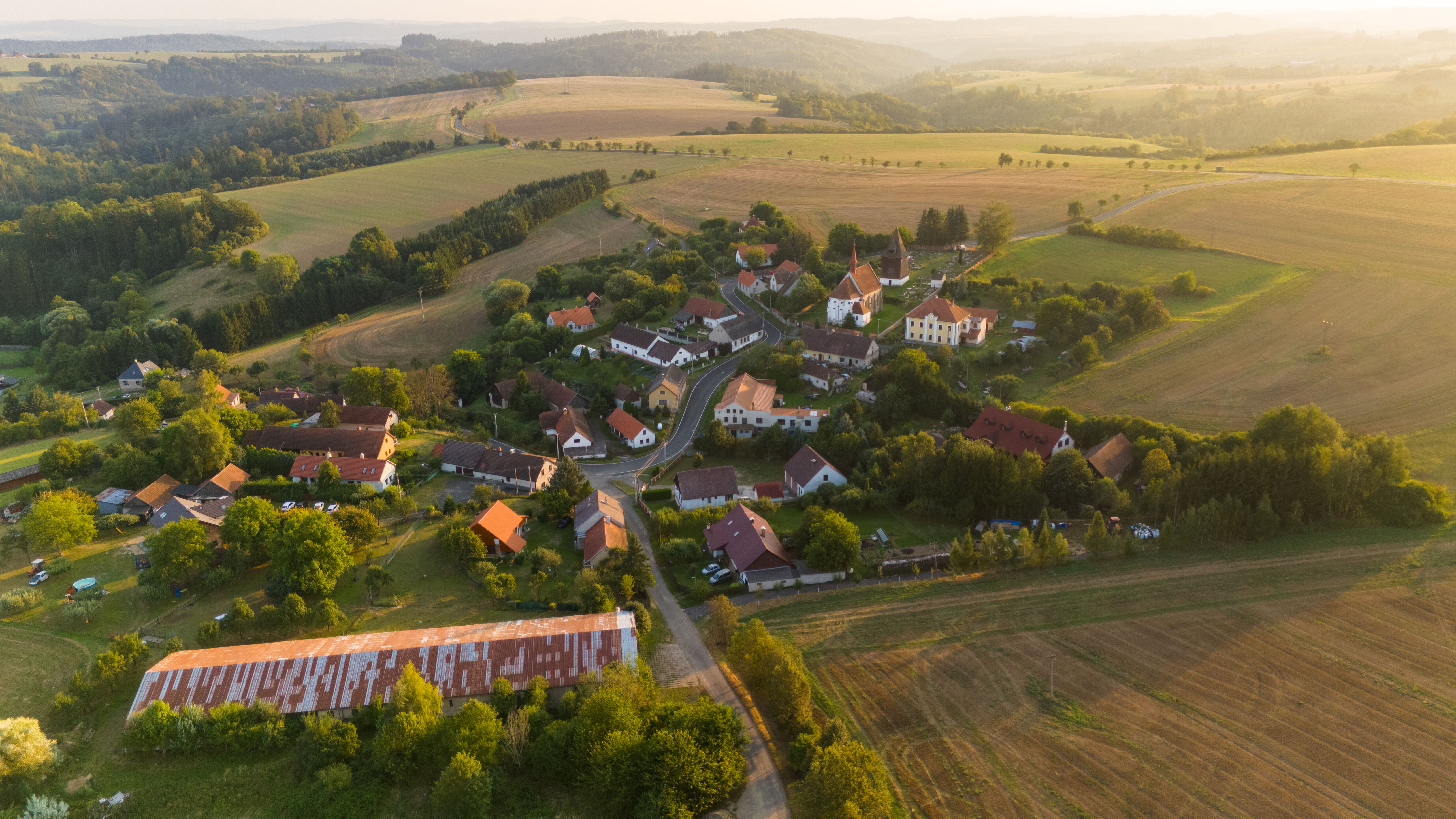Drone captures a picturesque village surrounded by farmland and rolling hills in Petrovice II, Česko.