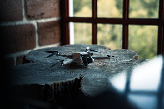A drone is resting on a rustic wooden table against a brick wall, illuminated by natural light.