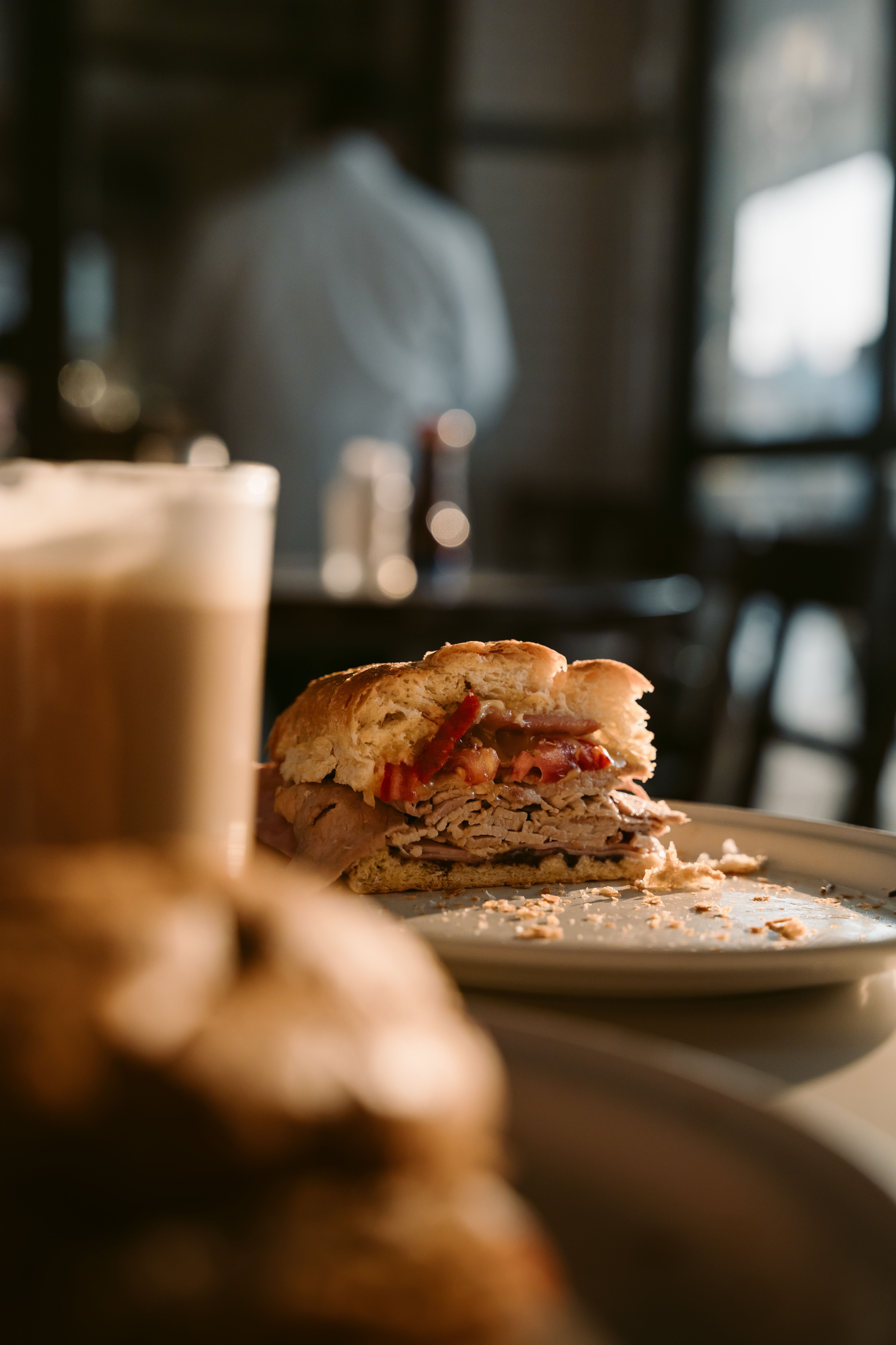 A delicious turkey sandwich with fresh vegetables and a coffee on a table in a cozy cafe.