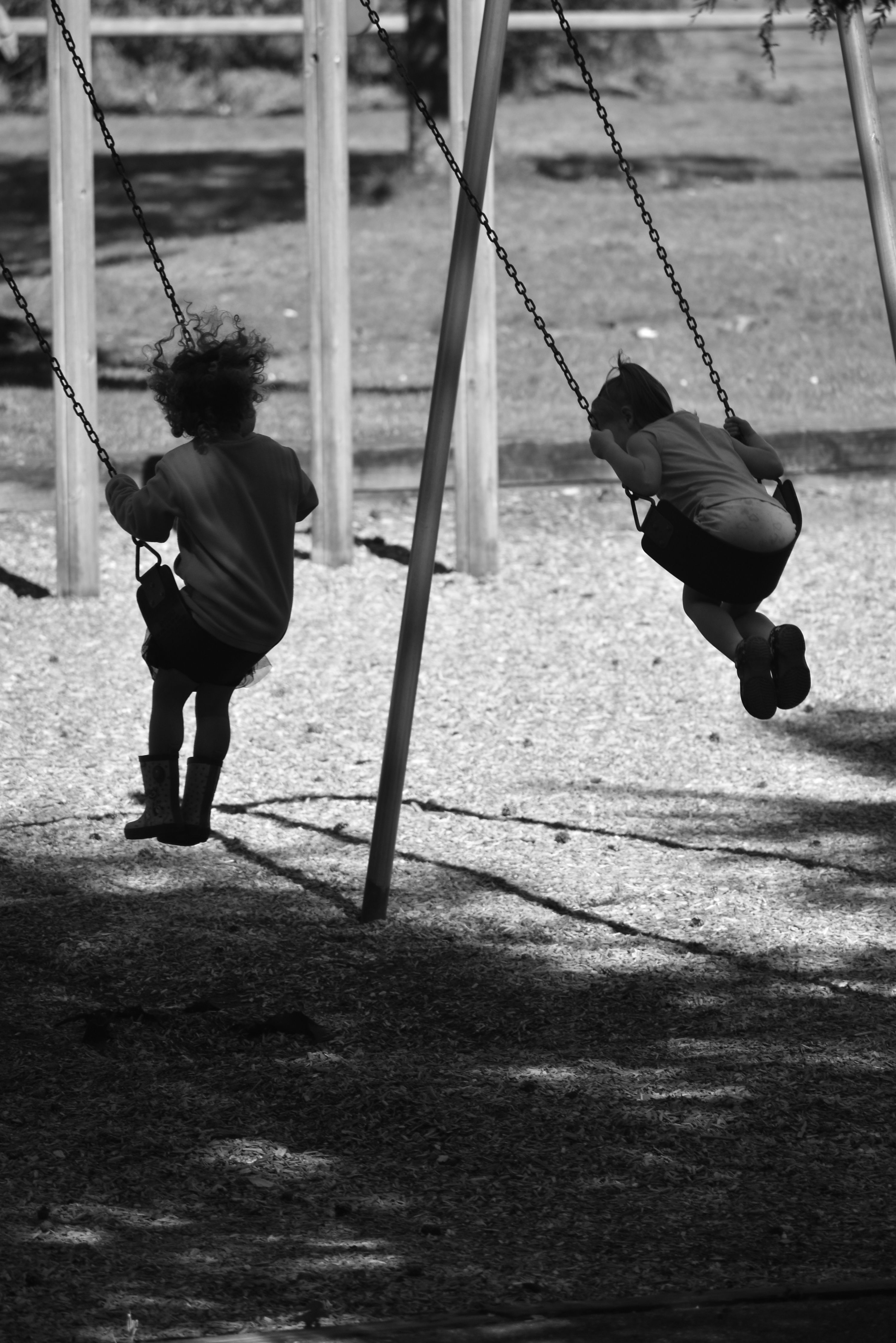 Black and white photo of children swinging joyfully at a park.