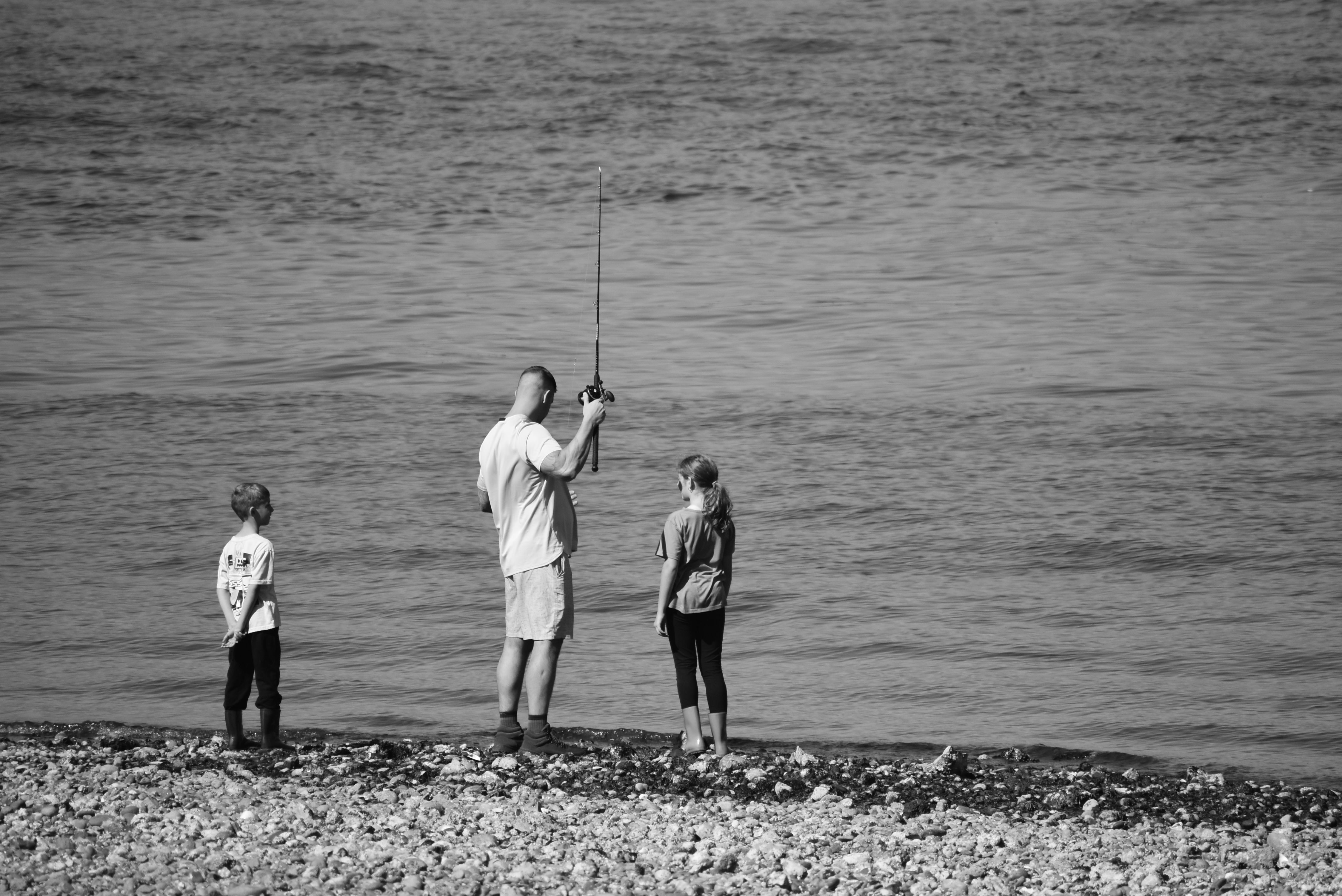 A family enjoys fishing together by the shoreline, captured in a black and white photograph.