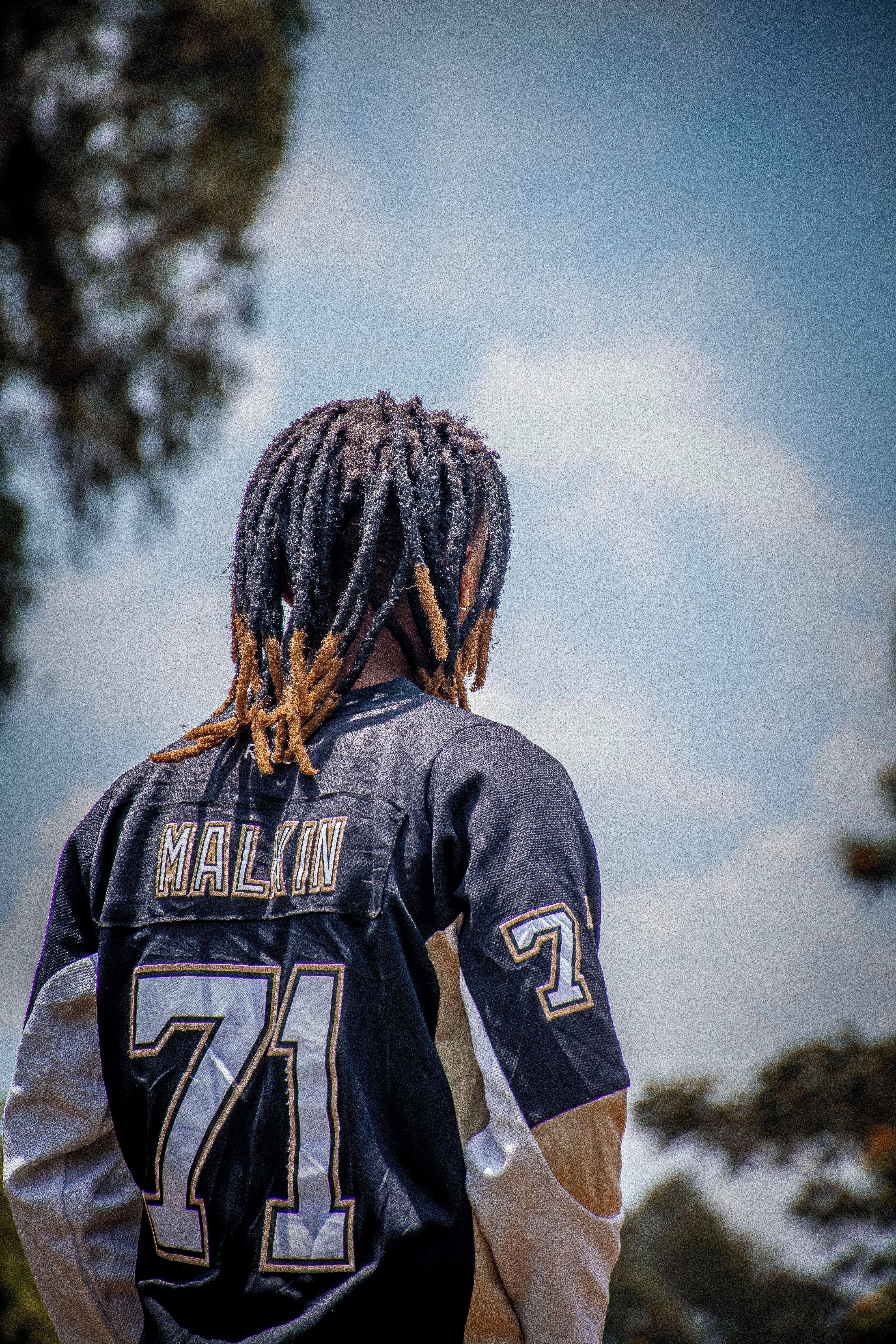 A person with dreadlocks wearing a Malkin 71 jersey, captured from behind.