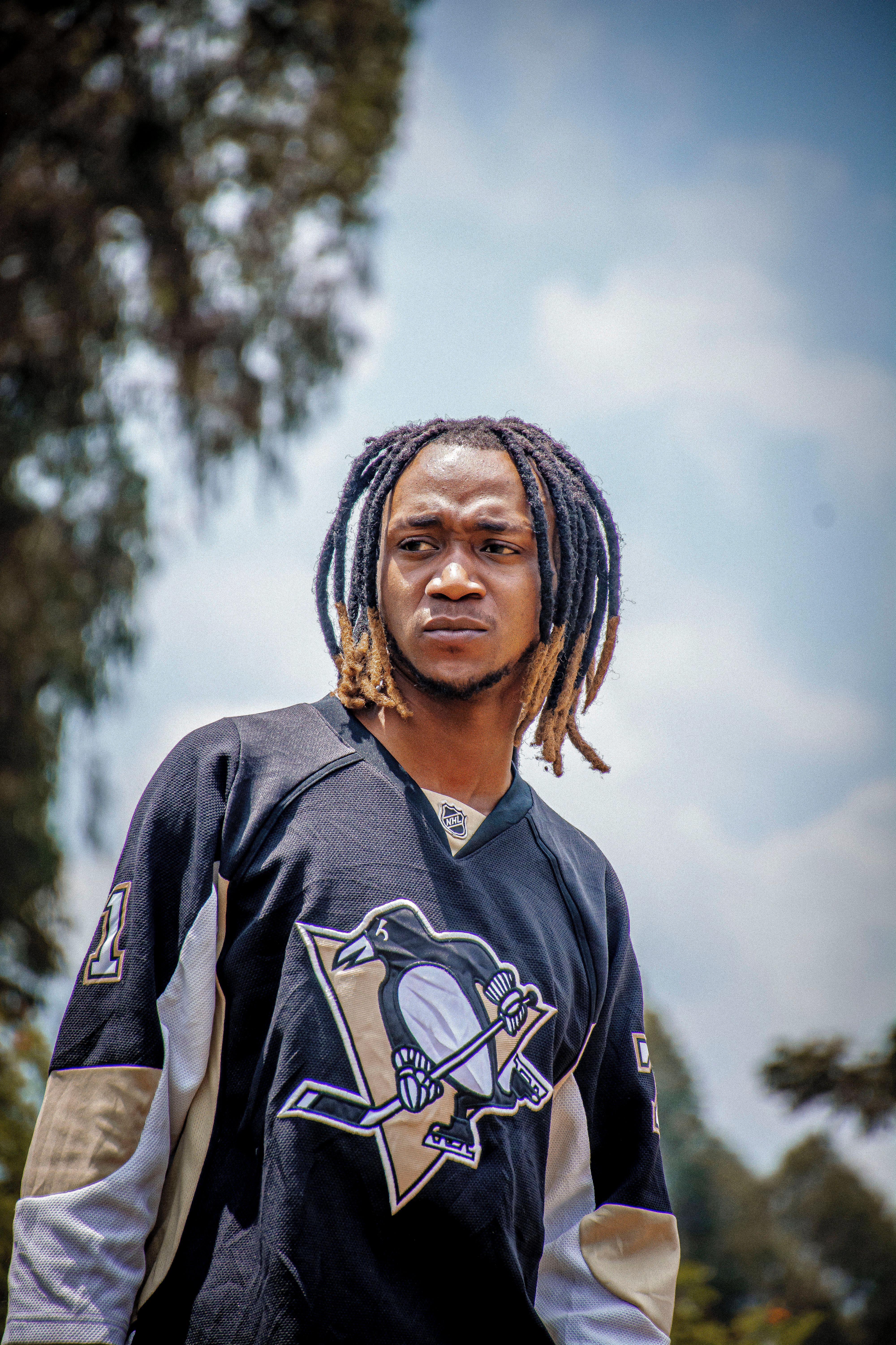 Young man with dreadlocks in a hockey jersey outdoors on a sunny day.