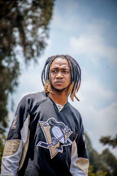 Young man with dreadlocks in a hockey jersey outdoors on a sunny day.