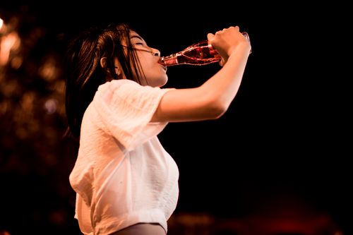 Free A woman in a white top drinks from a bottle outside at night, enjoying the refreshing beverage. Stock Photo